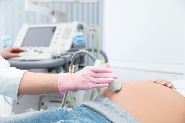 Young pregnant woman undergoing ultrasound scan in modern clinic - Fotó, kép