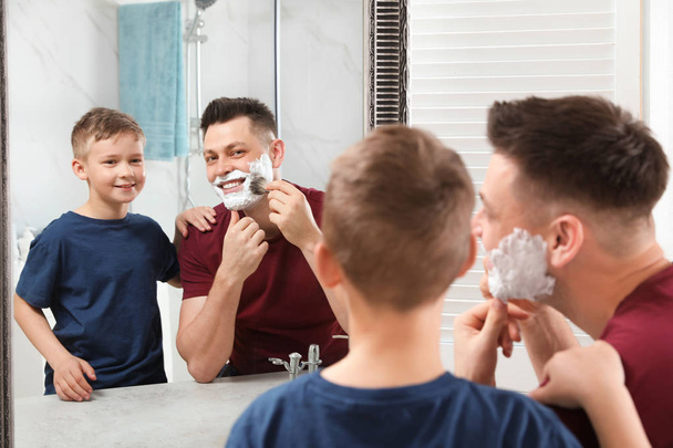 Dad applying shaving foam near son at mirror in bathroom - 写真・画像