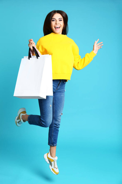 Happy young woman with paper bags jumping on blue background - Foto, Imagen