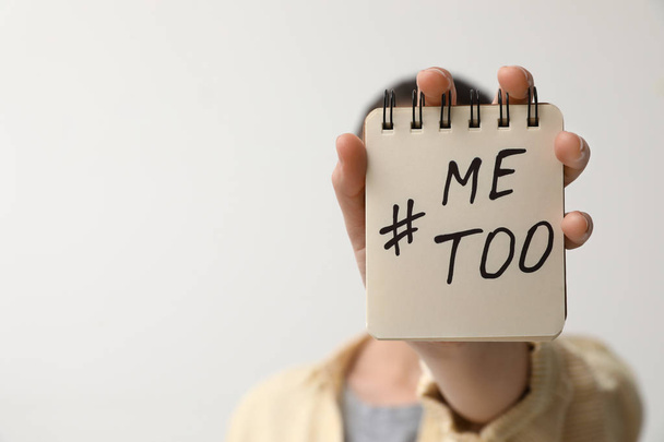 Woman holding notebook with hashtag MeToo against light background, closeup. Stop sexual assault - 写真・画像