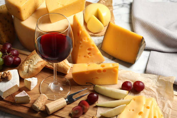 Board with different kinds of delicious cheese, snacks and wine on marble table - Foto, Imagen