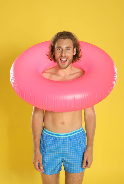 Attractive young man in swimwear with pink inflatable ring on yellow background - Fotó, kép