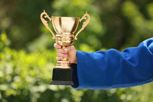 Young man in blue kimono with gold trophy cup outdoors, closeup - Foto, imagen