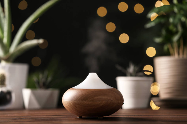 Composition with modern essential oil diffuser on wooden table against blurred lights, space for text - Foto, afbeelding