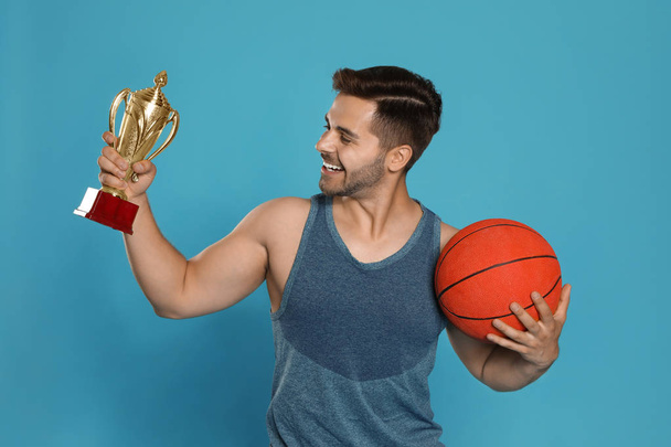Porträt eines glücklichen jungen Basketballspielers mit goldenem Pokal auf blauem Hintergrund - Foto, Bild