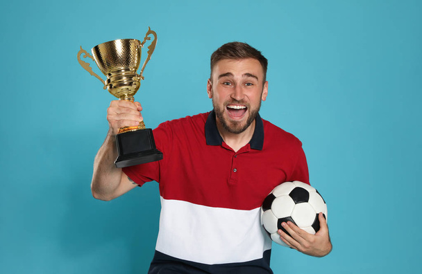 Portrait of happy young soccer player with gold trophy cup and ball on blue background - Valokuva, kuva