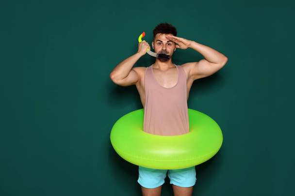 Funny young man with bright inflatable ring on dark green background - Fotoğraf, Görsel