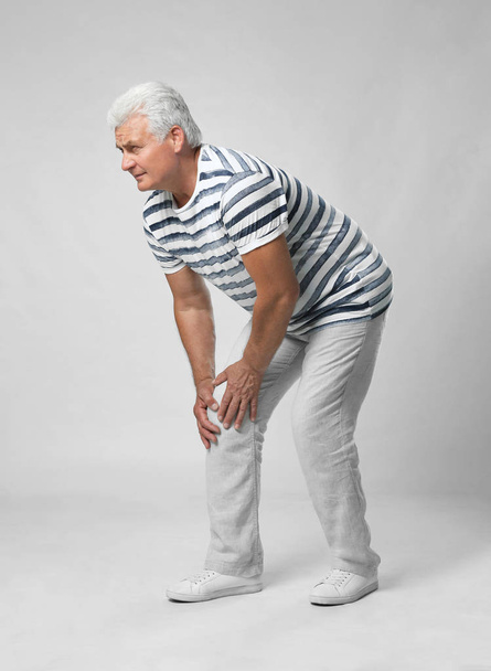 Full length portrait of senior man having knee problems on grey background - Foto, afbeelding