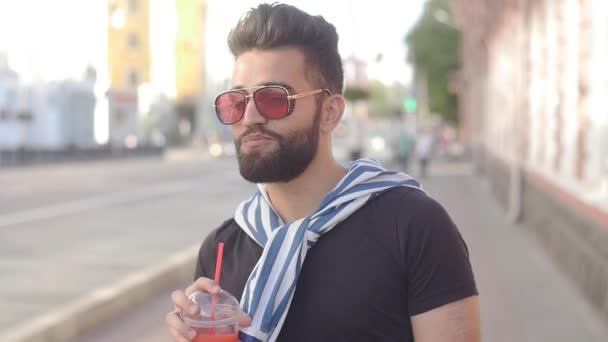 Concept of street food and city life. Young smiling bearded man holding a cup with drink juice smoothies or lemonade - Footage, Video