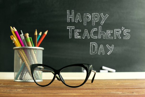 Brillenlehrer und ein Ständer mit Bleistiften auf dem Tisch, auf dem Hintergrund einer Tafel mit Kreide. das Konzept des Lehrertages. Kopierraum. - Foto, Bild