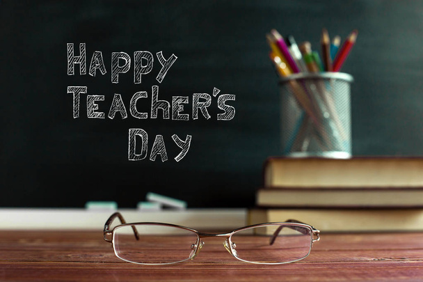 Glasses teacher books and a stand with pencils on the table, on the background of a blackboard with chalk. The concept of the teacher's day. Copy space. - 写真・画像