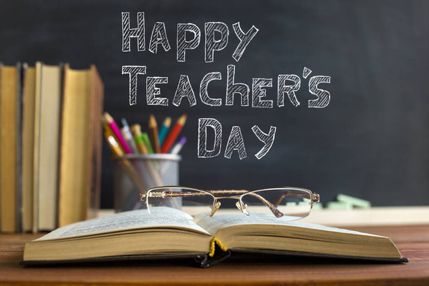 Glasses teacher books and a stand with pencils on the table, on the background of a blackboard with chalk. The concept of the teacher's day. Copy space. - Φωτογραφία, εικόνα