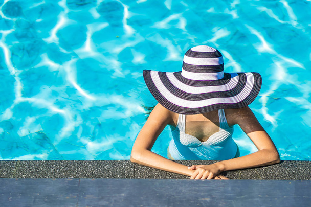 Όμορφη νεαρή Ασιατική γυναίκα με καπέλο στην πισίνα για ταξίδια - Φωτογραφία, εικόνα