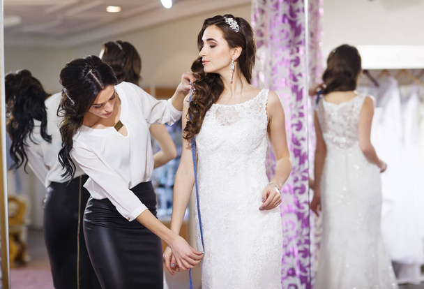 Female trying on wedding dress in a shop with women assistant. - 写真・画像