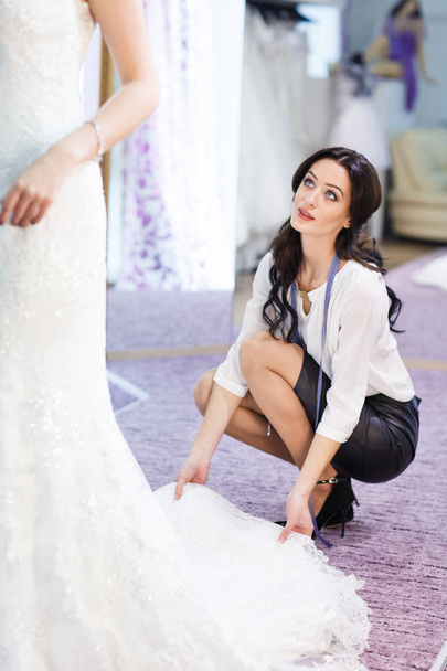 Female trying on wedding dress in a shop with women assistant. - Foto, Bild