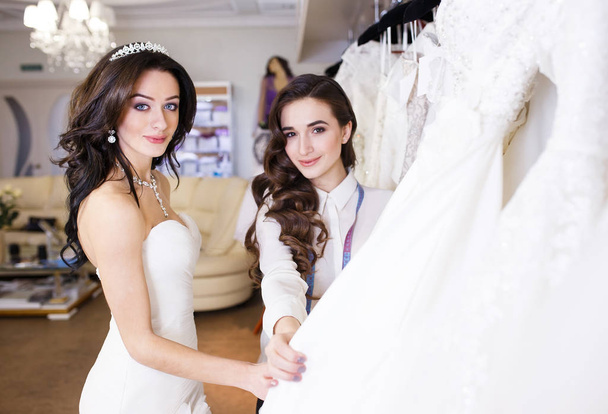 Female trying on wedding dress in a shop with women assistant. - Foto, Imagem