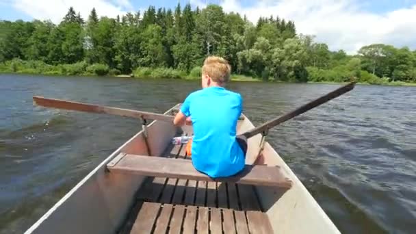Niño en azul con chalecos salvavidas en las piernas flota en el barco y el escaramujo duro. Joven en barco de metal navegar en el agua del lago
 - Metraje, vídeo
