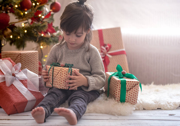 La niña bonita sostiene una caja de regalo y sonríe mientras está sentada en su cama en su habitación en casa
 - Foto, imagen