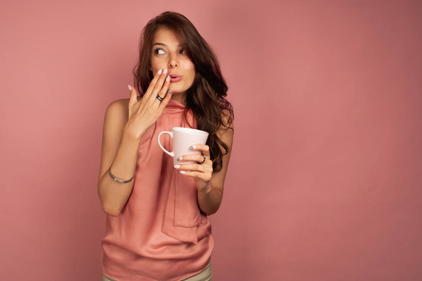 Joven morena quiere contar un secreto mientras bebe té o café
 - Foto, Imagen