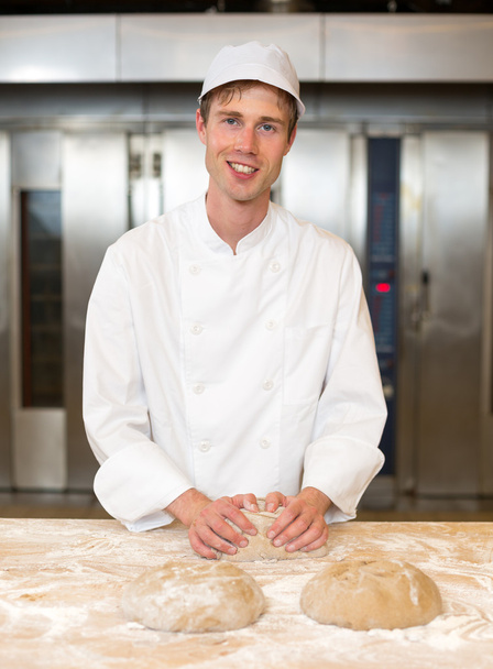 Smiling baker kneading dough in bakery - Valokuva, kuva