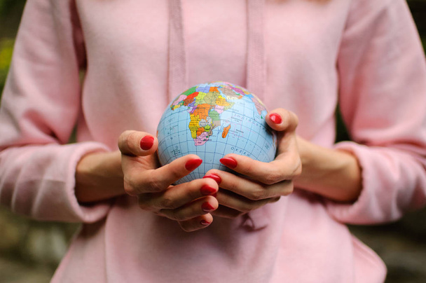 Female hands with a small globe with Ukrainian names and Cyrillic letters on it. African continent is visible. Environmental issues concept. - Photo, Image