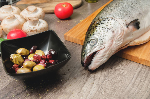 クローズアップケタ魚、オリーブトマトとキノコの隣の台所のテーブルのまな板の全体。健康的なシーフード。自家製料理 - 写真・画像