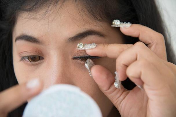Closeup portrait of pretty Asian woman sticks false eyelashes of herself.  - Фото, зображення
