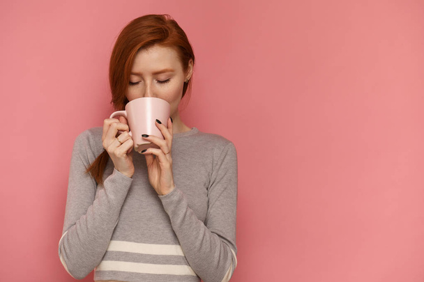 Redhead young woman with a cup enjoys her hot drink - Foto, Imagen