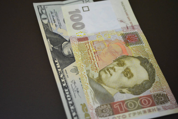 Χαρτονομίσματα σε μέγεθος $20 USD είκοσι αμερικάνικα δολάρια και € 100 100 ουκρανικό ευρώ σε ένα καφέ ματ φόντο. Ουκρανικές και αμερικανικές νομισματικές μονάδες, πληρωμές και πληρωμές σε μετρητά. - Φωτογραφία, εικόνα