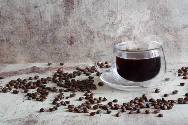 Gorąca kawa w pięknej przezroczystej filiżance, ziarna kawy rozproszone na szarym tle - Zdjęcie, obraz