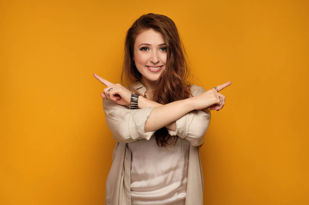 Young woman with long hair points at opposite sides crossing her hands, yellow background - Foto, Imagen