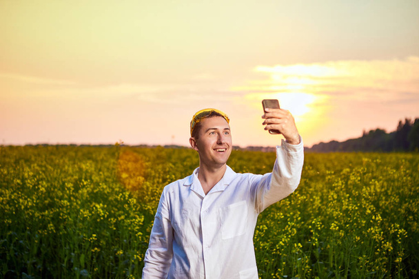 Agronomist man of boer inspecteren kwaliteit van koolzaad veld en het nemen van foto met mobiele telefoon - Foto, afbeelding