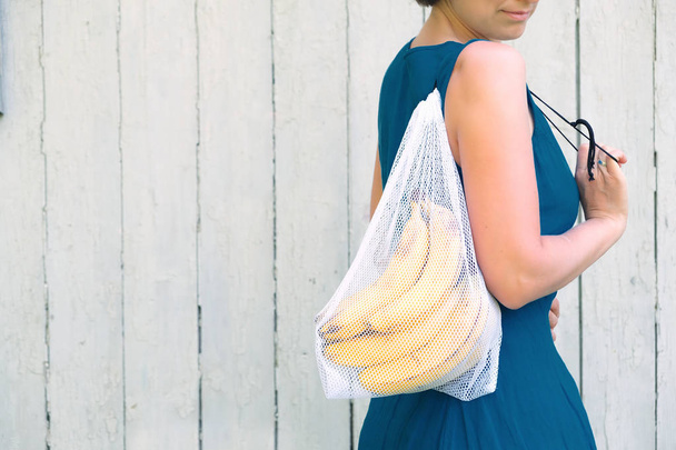 Zero waste shopping concept. No single use plastic. Woman holding reusable recycled mesh produce bag with bananas.  - Fotoğraf, Görsel