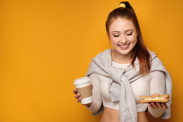 Молодая женщина с конским хвостом улыбается, держа еду на желтом фоне
 - Фото, изображение