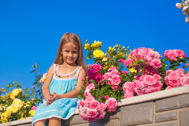 kleines entzückendes Mädchen, das an einem Sommertag neben bunten Blumen sitzt - Foto, Bild
