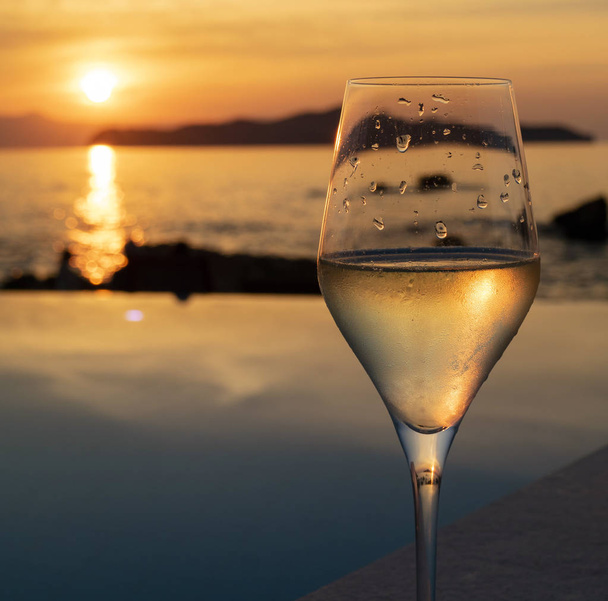 Kreta, Grecja. 2019 czerwca. Słońce zejściem na małą wyspę widzianą przez kieliszek wina musującego. - Zdjęcie, obraz