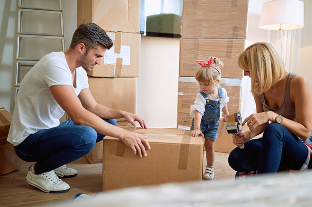 Young Family unpacking cardboard boxes in their new home - Фото, изображение