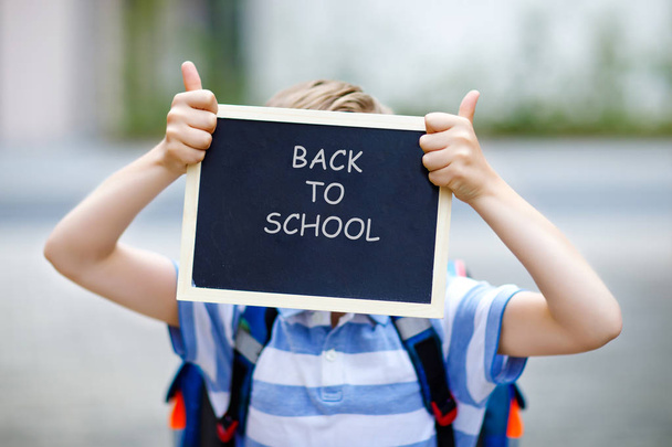 Happy little kid boy with backpack or satchel. Schoolkid on the way to school. Healthy adorable child outdoors With chalk desk for copyspace. Back to school or schools out. Unrecognizable face - Photo, Image