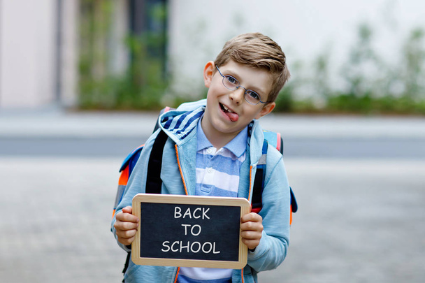 Menino feliz com mochila ou mochila e óculos. Um estudante a caminho da escola. Criança adorável saudável ao ar livre. Na mesa de giz De volta à escola
 - Foto, Imagem