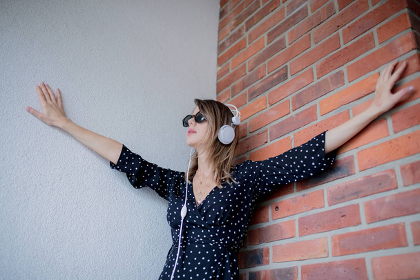 Frau mit Kopfhörern und Sonnenbrille vor Backsteinmauer-Hintergrund - Foto, Bild
