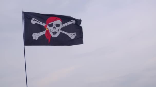 Пиратский флаг Веселый Роджер висит на мачте корабля на голубом фоне неба в ветреный день
. - Кадры, видео
