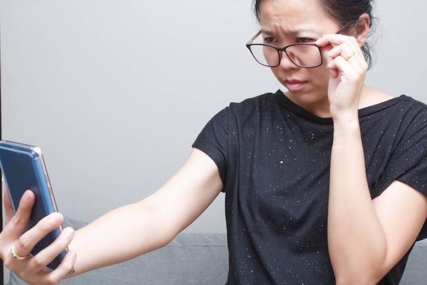 Asian kobieta próbuje przeczytać coś w jej telefon komórkowy. słaby wzrok, dalekowzroczność, krótkowzroczności - Zdjęcie, obraz