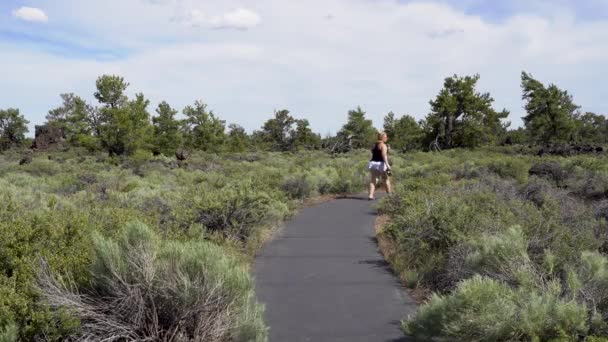 Escursionista bionda cammina lungo il sentiero Devils Orchard in Craters of the Moon National Monument vicino ad Arco, Idaho. Sagebrush deserto e roccia vulcanica circondato il sentiero asfaltato
 - Filmati, video