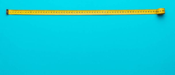 Top view of yellow measuring tape over turquoise blue background with copy space - Photo, image