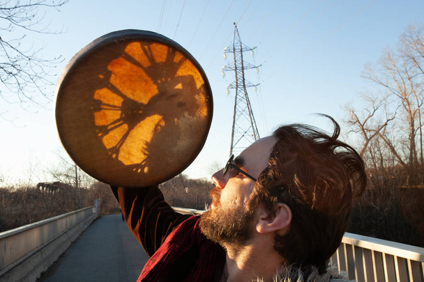 Spiritual man holds sacred drum to sun - Photo, Image