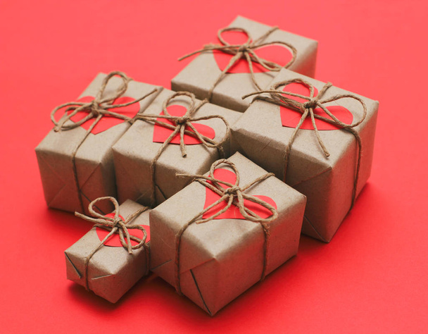 Set of brown gift boxes. Wrapped in craft paper and tied by hemp cord. Bright red background and carton hearts decorative card.  - Φωτογραφία, εικόνα