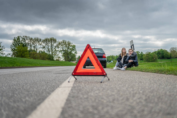 Dos mujeres con la avería del coche sentadas en la carretera y esperando ayuda
 - Foto, imagen