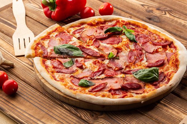 Pizza met ham, warme worst, salami en mozzarella op houten achtergrond close-up. Italiaanse gerechten. Pizza met prosciutto en salami op houten tafel. Top View. - Foto, afbeelding