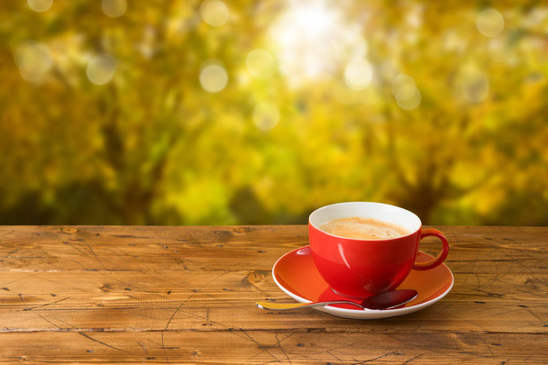 Red coffee cup on wooden table over autumn bokeh background - Photo, Image