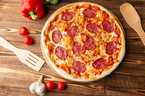 Ahşap masada lezzetli sıcak ev yapımı Pepperoni pizza. Pepperoni Pizza - Kopya alanı ile rustik siyah taş arka plan üzerinde pepperoni, peynir ve domates soslu taze ev yapımı pizza. - Fotoğraf, Görsel